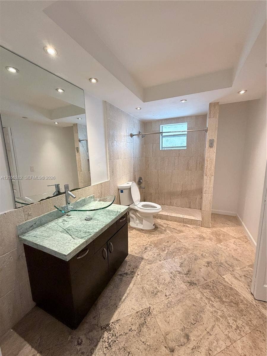 665 NE 83rd Terrace, #210, Miami, Miami, FL 33138 Bathroom featuring stone tile flooring and shower surround, dark wood-finish vanity with a stone countertop, glass vessel sink, and recessed ceiling lighting