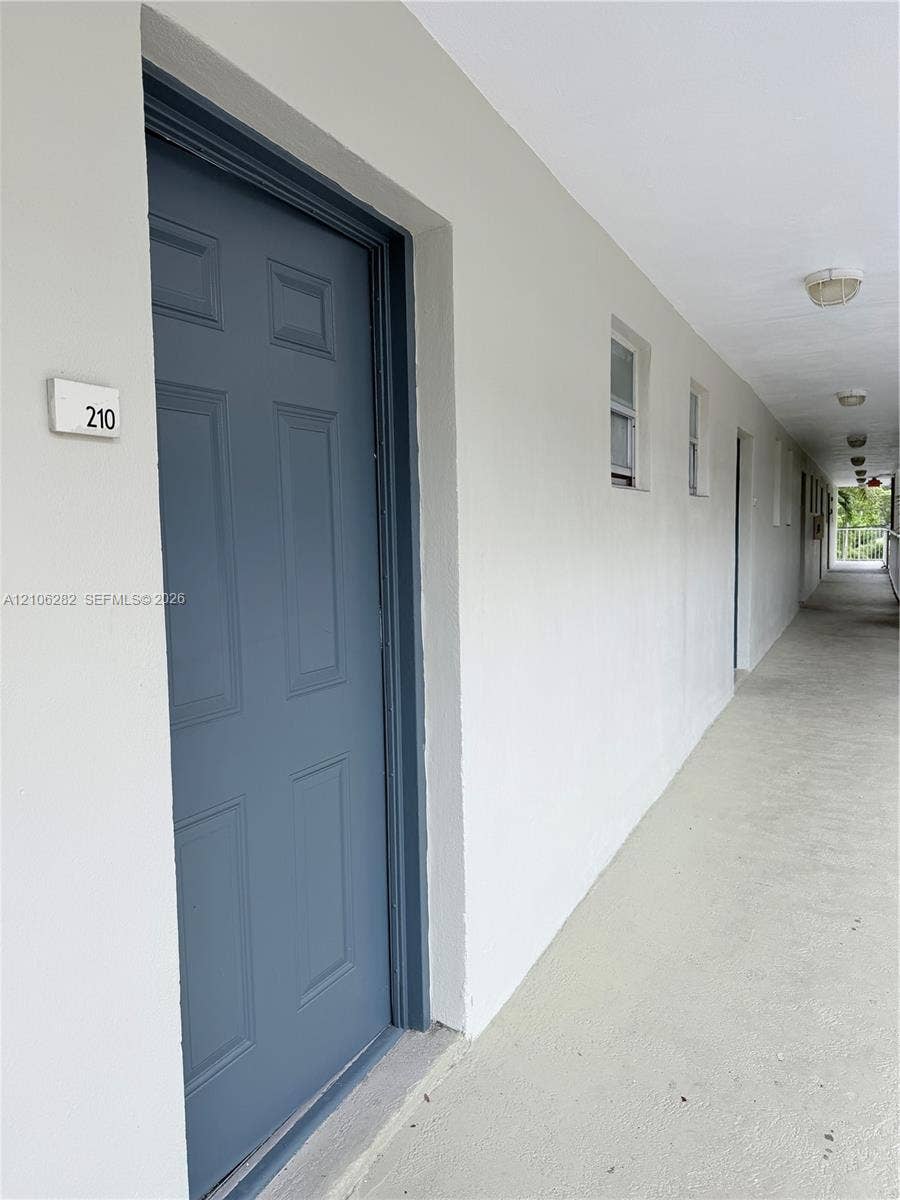 665 NE 83rd Terrace, #210, Miami, Miami, FL 33138 Exterior entrance featuring a paneled door, flush-mounted wall lighting, and concrete-finish walkway