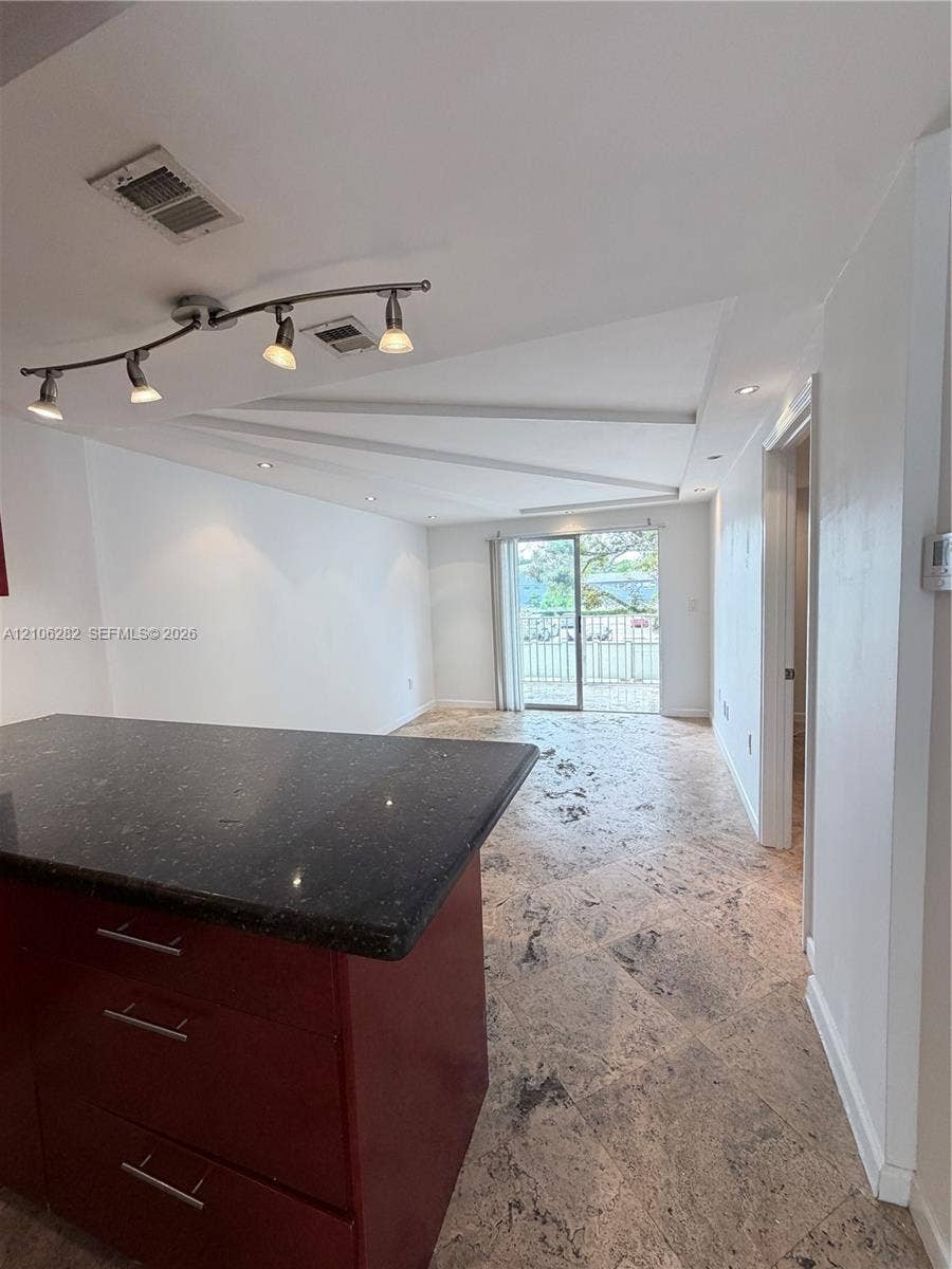 665 NE 83rd Terrace, #210, Miami, Miami, FL 33138 Stone-tile flooring throughout, kitchen island with dark stone countertop, recessed ceiling lighting, multi-bulb adjustable track lighting, and sliding glass door