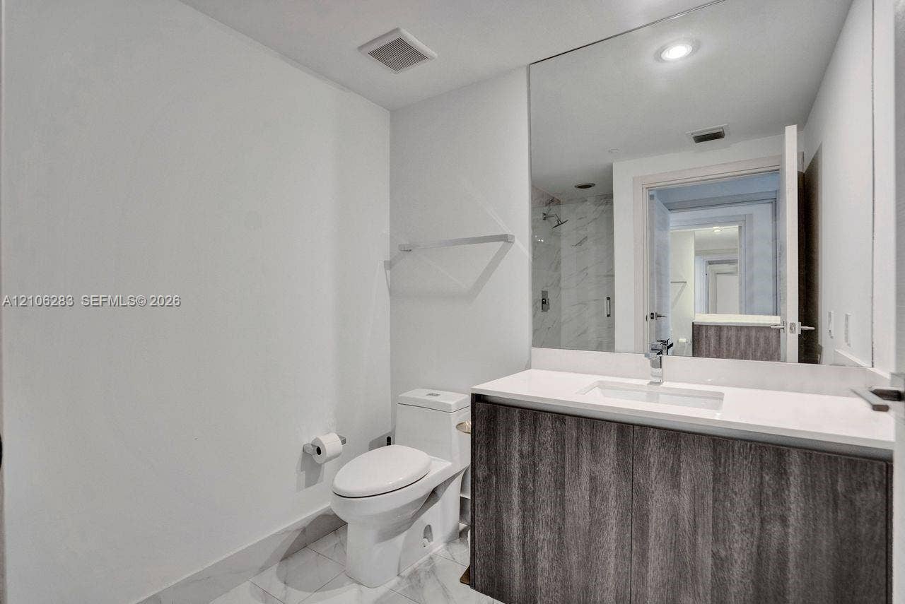801 S Miami Avenue, #1801, Miami, FL 33130 Modern vanity with dark wood-finish cabinetry, crisp white countertop, integrated rectangular sink, expansive wall-to-wall mirror, and stone-finish tile flooring