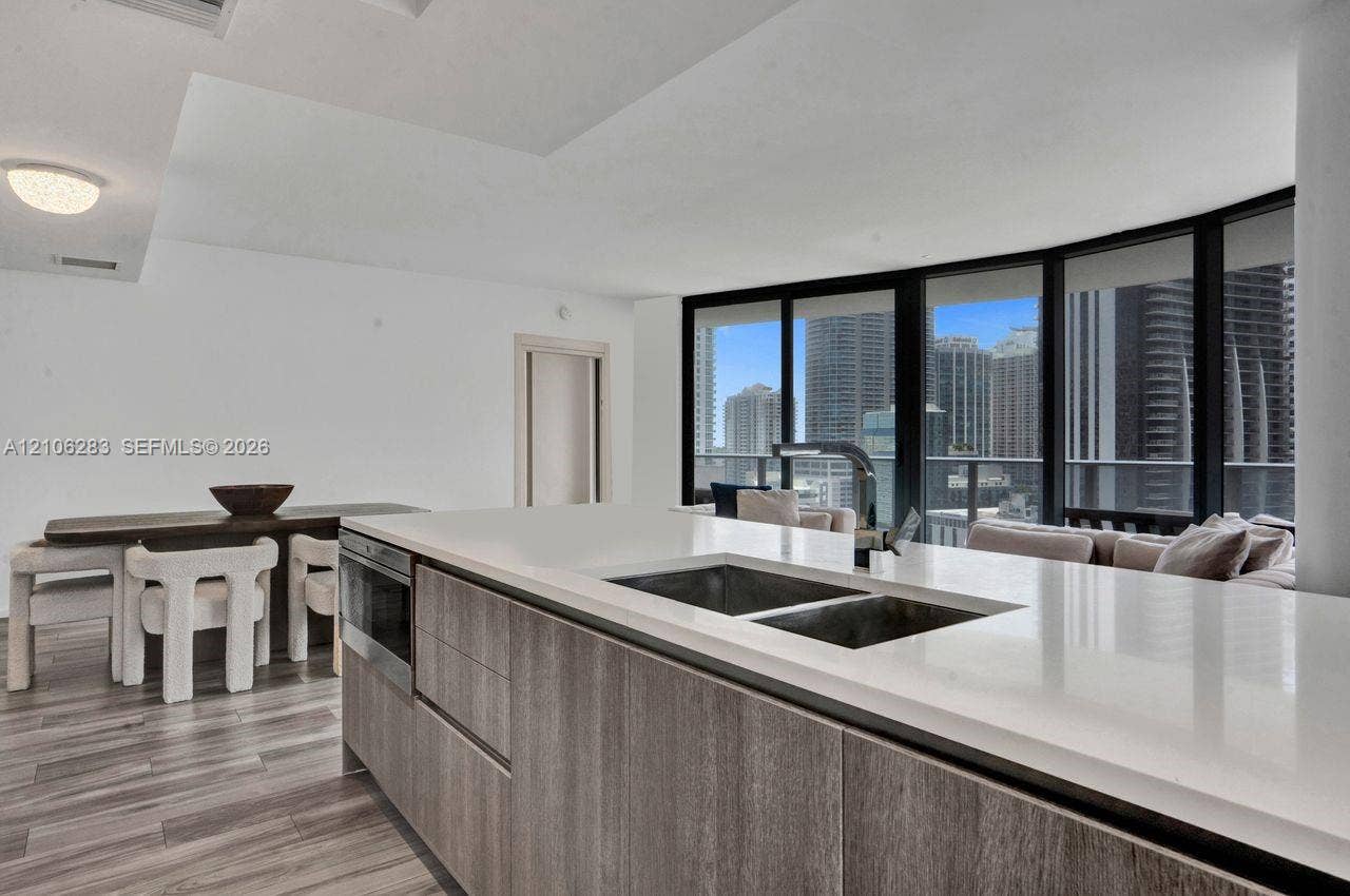 801 S Miami Avenue, #1801, Miami, FL 33130 Kitchen island featuring wood-finish cabinetry, a solid surface countertop, an undermount double-basin sink, and a gooseneck faucet, set against floor-to-ceiling windows with urban scenery