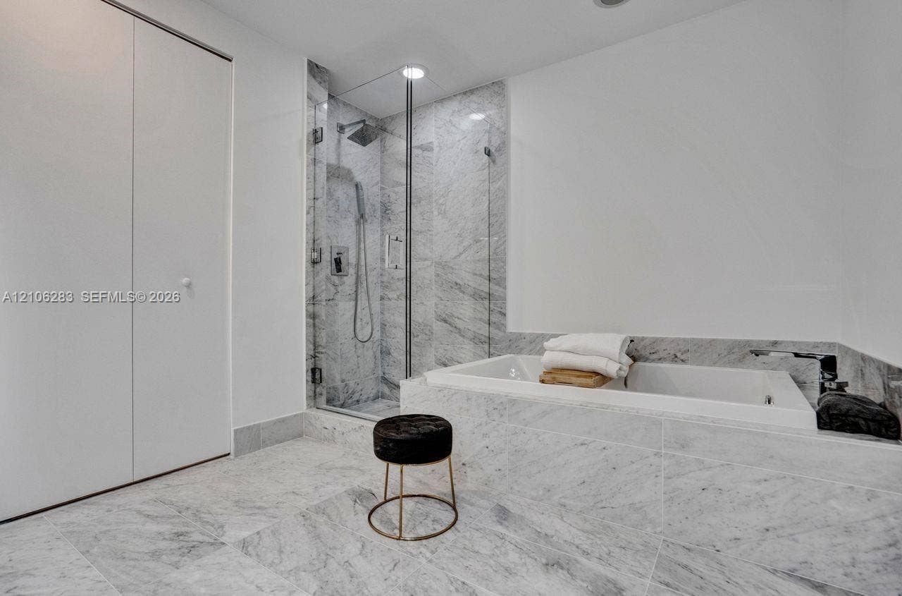 801 S Miami Avenue, #1801, Miami, FL 33130 Stone-tiled bathroom featuring a walk-in shower with a glass enclosure, a deep soaking tub with stone surround, and recessed lighting