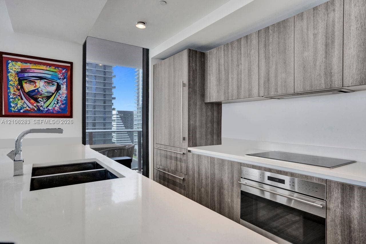 801 S Miami Avenue, #1801, Miami, FL 33130 Kitchen featuring flat-panel wood-finish cabinetry, integrated stainless steel appliances, white solid-surface countertops, and a full-height floor-to-ceiling glass window