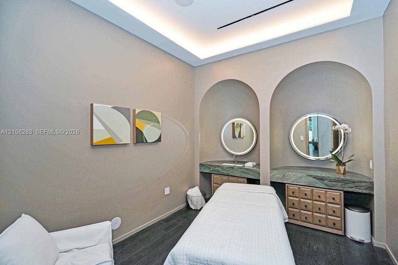 801 S Miami Avenue, #1801, Miami, FL 33130 Dual arched wall recesses featuring stone-topped built-in vanities, recessed tray ceiling with integrated perimeter lighting, round back-lit mirrors, and dark-toned plank flooring
