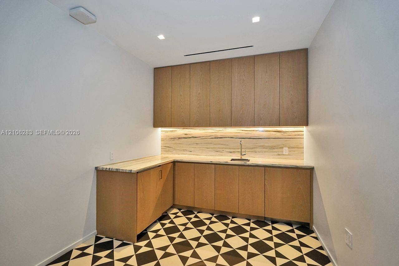 801 S Miami Avenue, #1801, Miami, FL 33130 L-shaped cabinetry featuring flat-panel wood-finish doors, stone-material countertops and backsplash, integrated under-cabinet lighting, and a metal sink faucet with geometric patterned floor tile