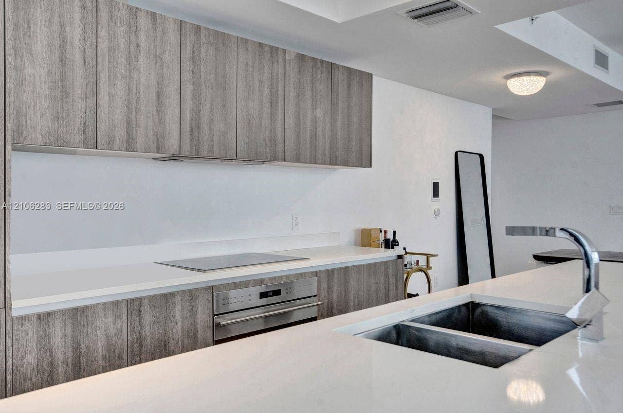 801 S Miami Avenue, #1801, Miami, FL 33130 Kitchen featuring grey-toned wood-finish cabinetry, white composite countertops, a stainless steel wall oven, an integrated cooktop, and an undermount double-basin sink with a chrome faucet