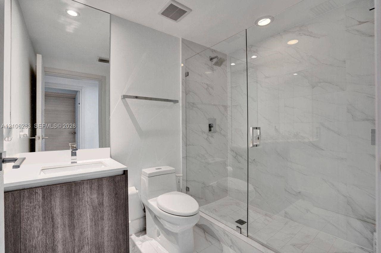 801 S Miami Avenue, #1801, Miami, FL 33130 Bathroom featuring a vanity with wood-finish cabinetry, a white countertop, a walk-in shower with a glass enclosure, floor-to-ceiling stone-style tile, and recessed lighting