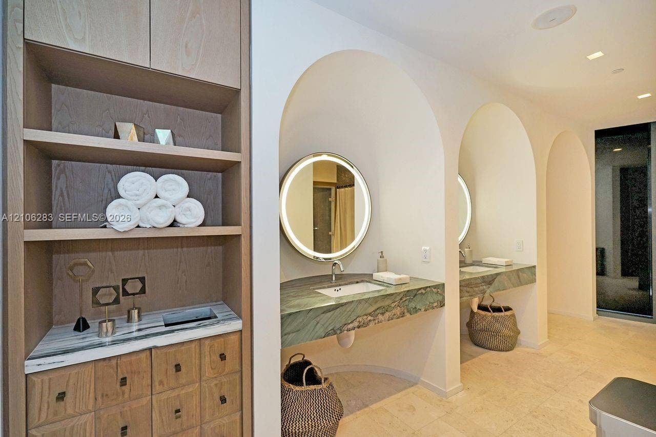 801 S Miami Avenue, #1801, Miami, FL 33130 Custom wood-finish built-in cabinetry, stone-topped floating vanities recessed within arched alcoves, circular backlit mirrors, and natural stone tile flooring