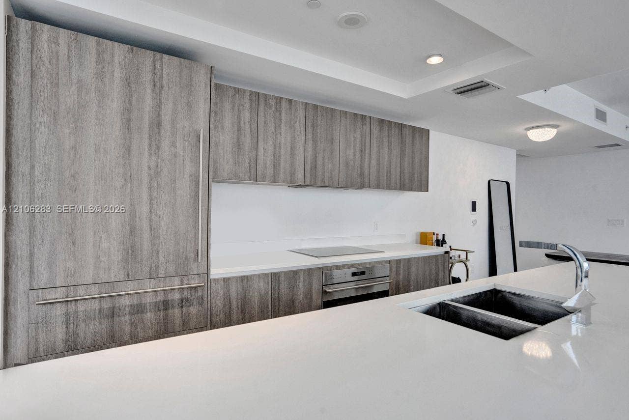 801 S Miami Avenue, #1801, Miami, FL 33130 Kitchen featuring wood-finish cabinetry, integrated panel-ready refrigerator, solid-surface countertops, stainless steel wall oven and cooktop, and an undermount double-basin sink with a chrome faucet