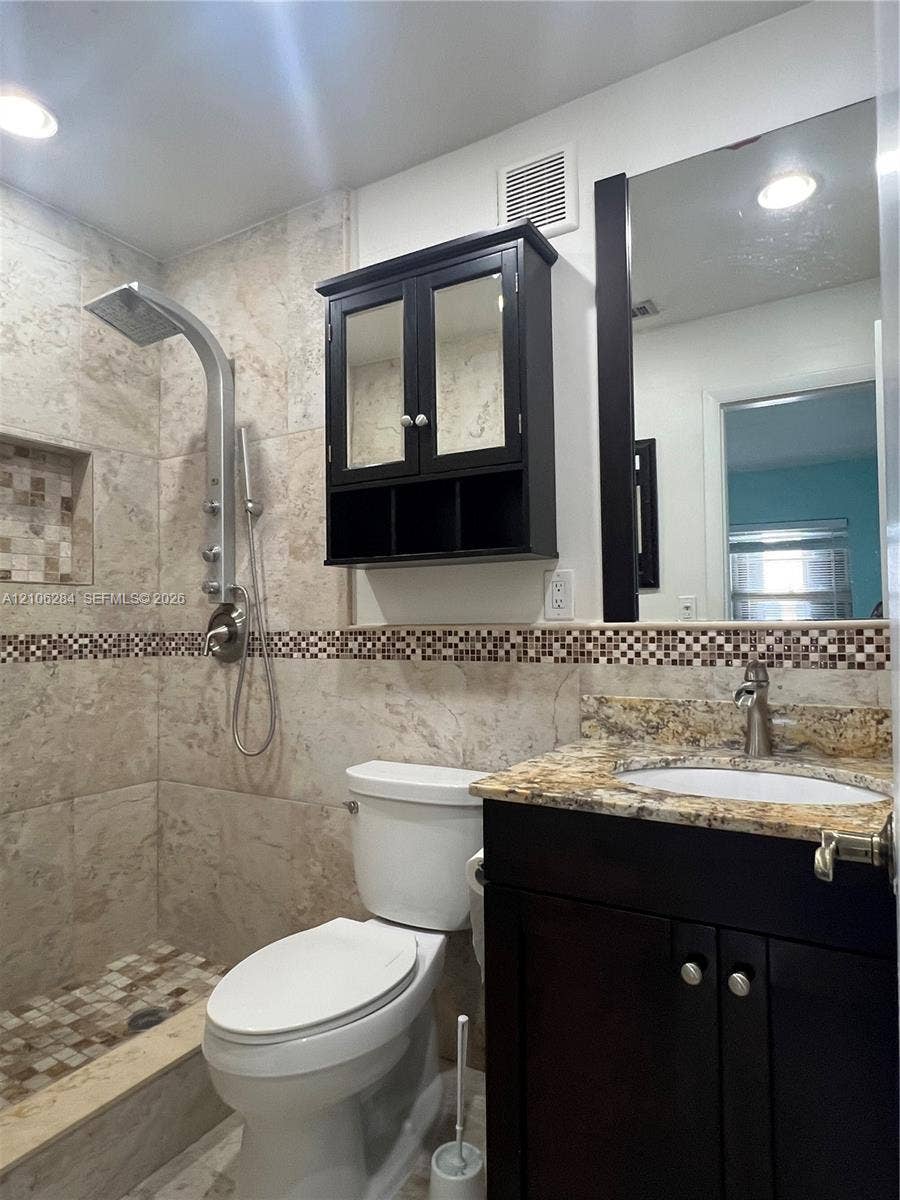11824 SW 123rd Avenue, #., Miami, Miami, FL 33186 Full-tile shower stall with integrated recessed shelving, multi-head shower system, stone-finish vanity countertop with undermount sink, dark-finish cabinetry, and framed mirror