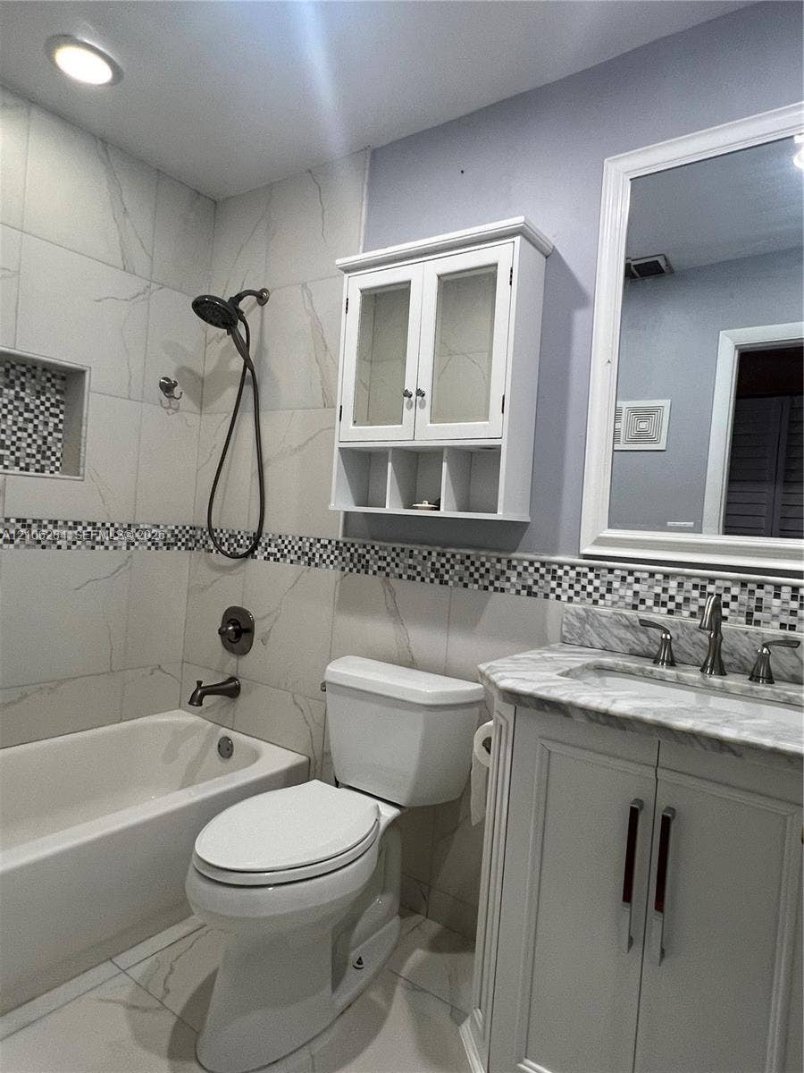 11824 SW 123rd Avenue, #., Miami, Miami, FL 33186 Bathroom featuring large-format light-toned tile walls, recessed shower niche with mosaic tile inlay, vanity with stone-finish countertop, mounted cabinetry, and framed mirror