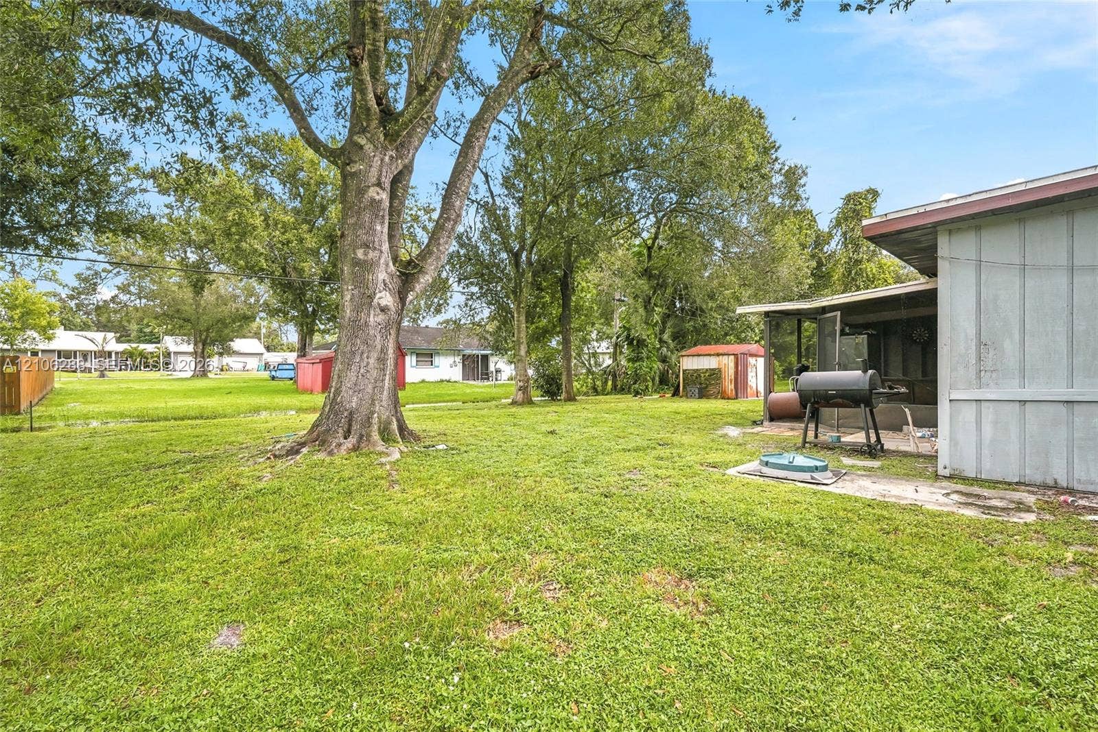 Expansive backyard featuring mature shade trees, a covered patio, and a storage shed