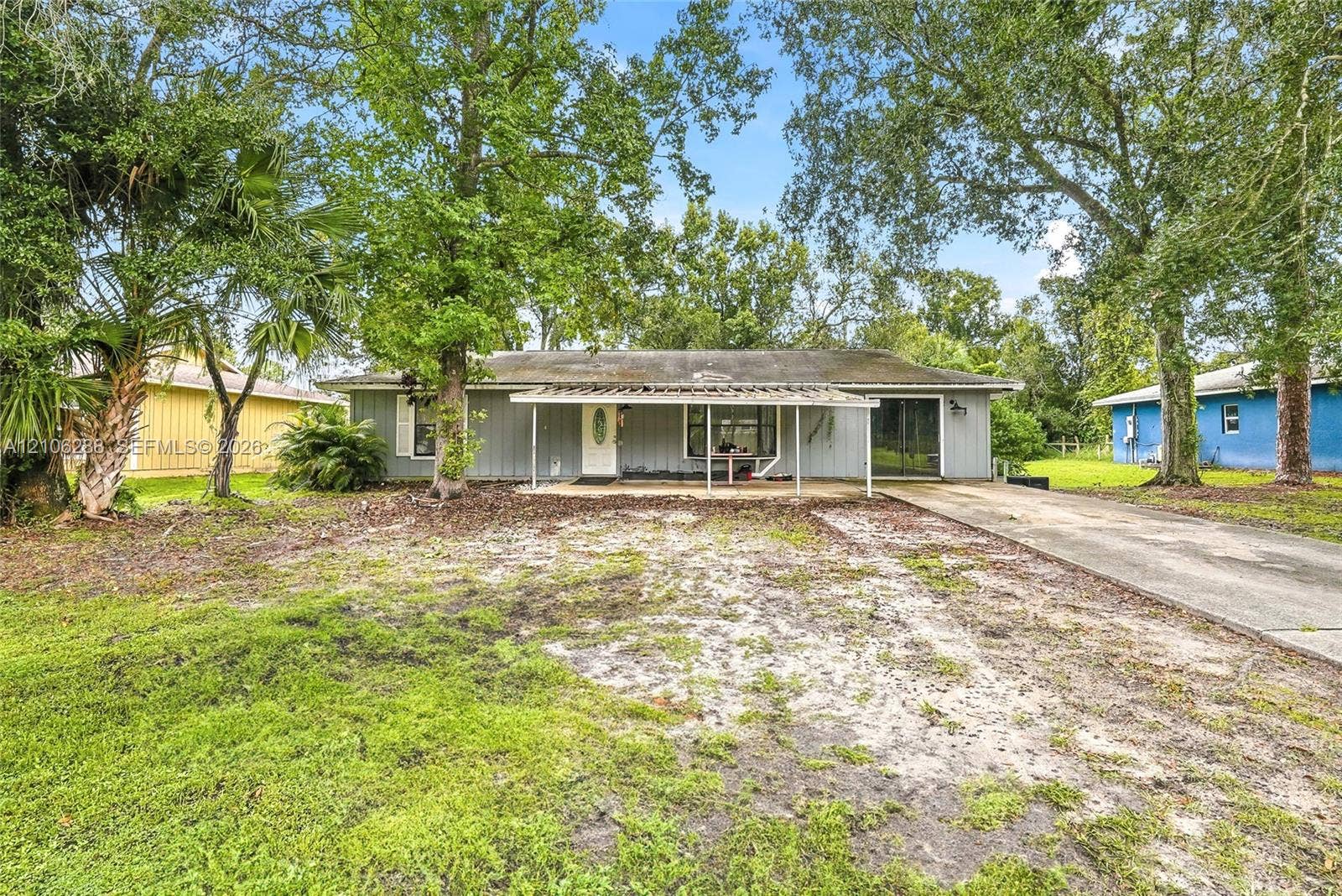 Single-story exterior featuring vertical siding, a front covered porch, and a concrete driveway, set on a lot with mature trees