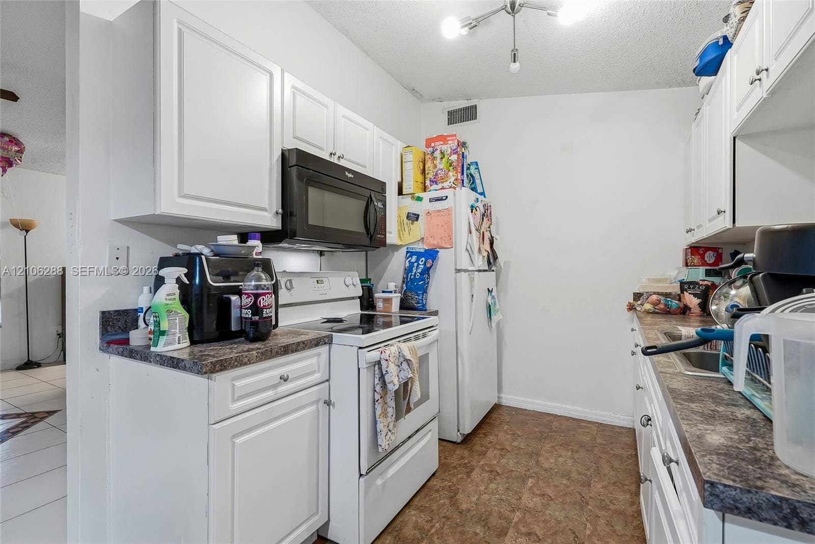 Kitchen featuring white cabinetry, dark stone-finish countertops, over-the-range microwave, white appliances, and tiled flooring