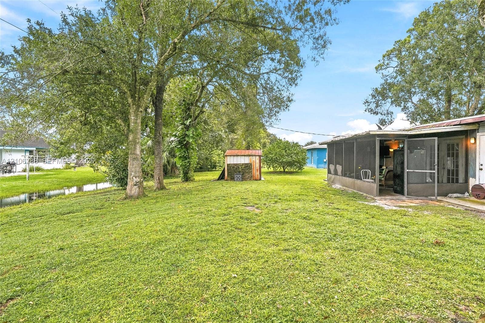 Expansive backyard featuring mature trees, a screened-in porch, and a detached wooden storage shed