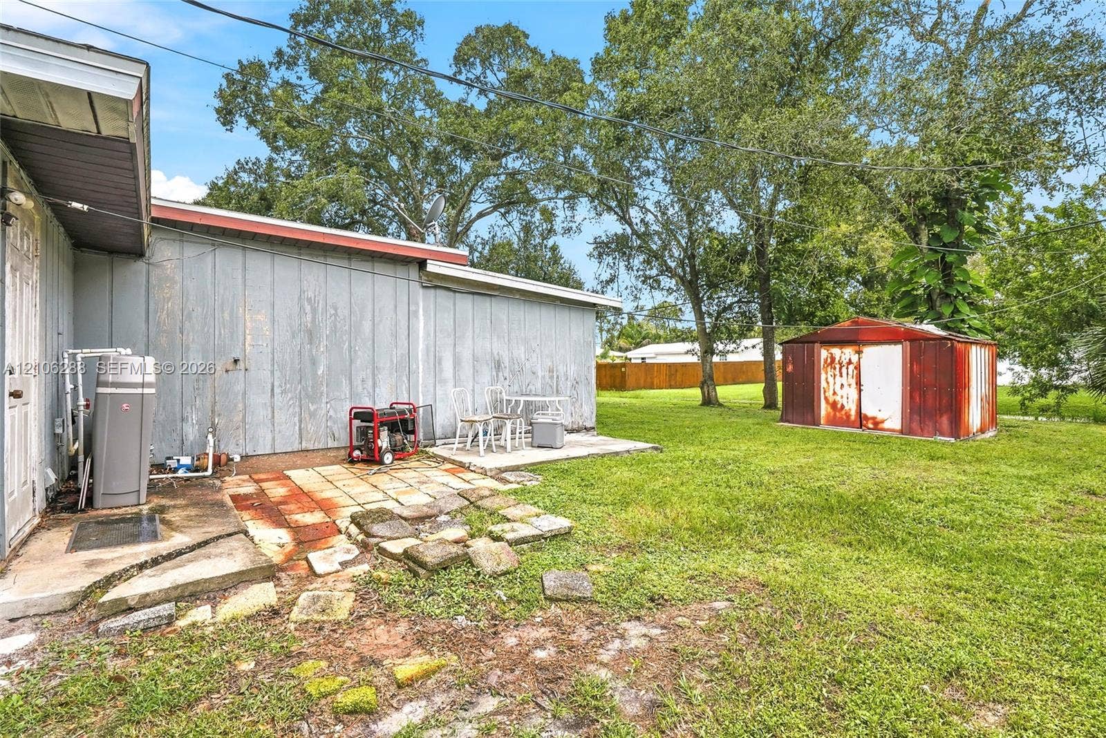 Expansive rear yard featuring mature trees, a detached metal storage structure, and a concrete patio area
