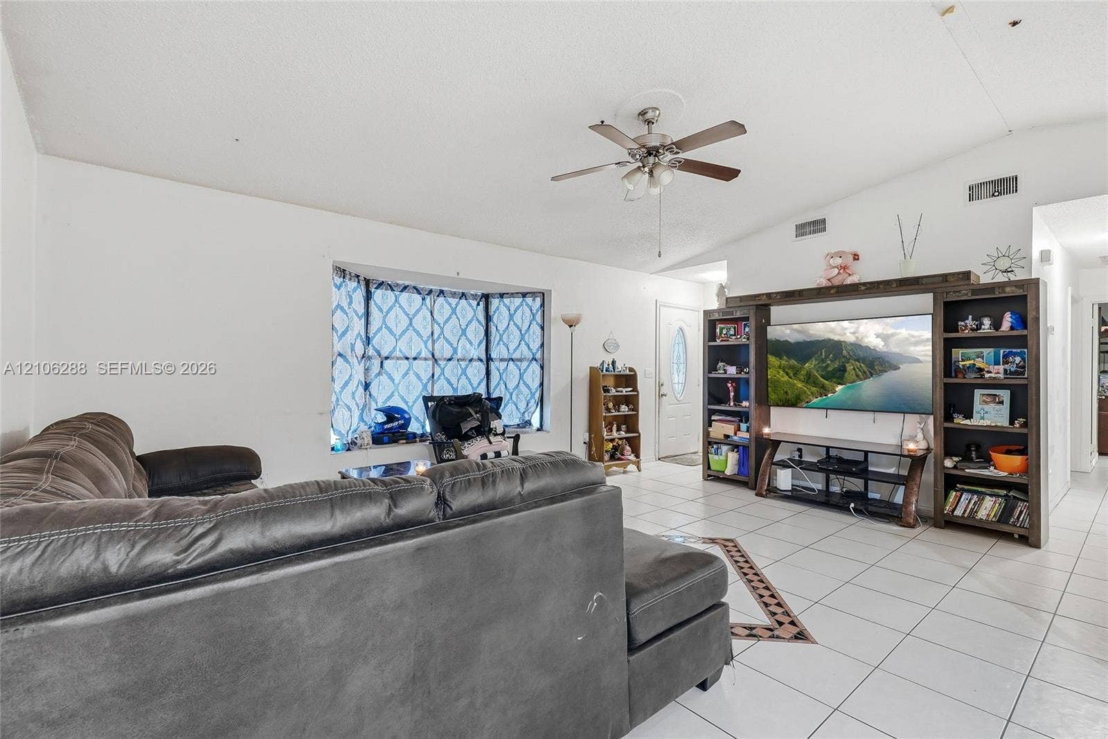 Living area featuring a vaulted ceiling, tile flooring, bay window, and a built-in media center with shelving
