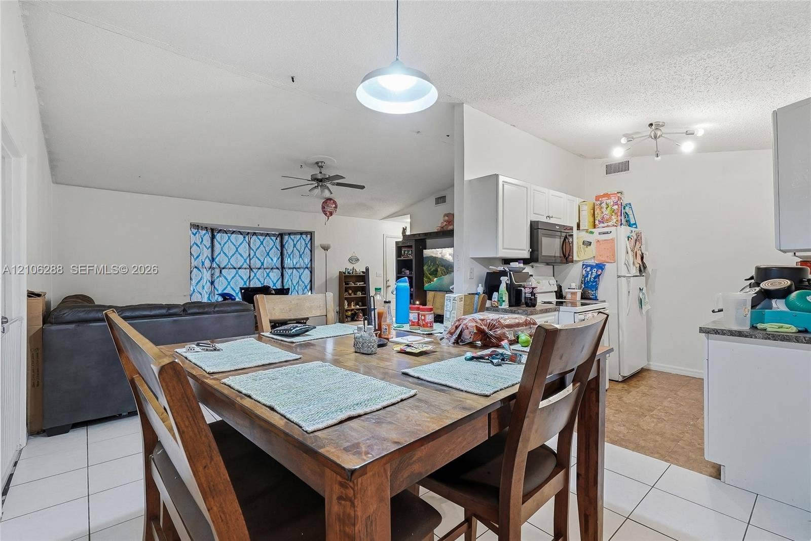 Vaulted ceilings, kitchen featuring white cabinetry, pendant lighting, ceiling fan, and bay window