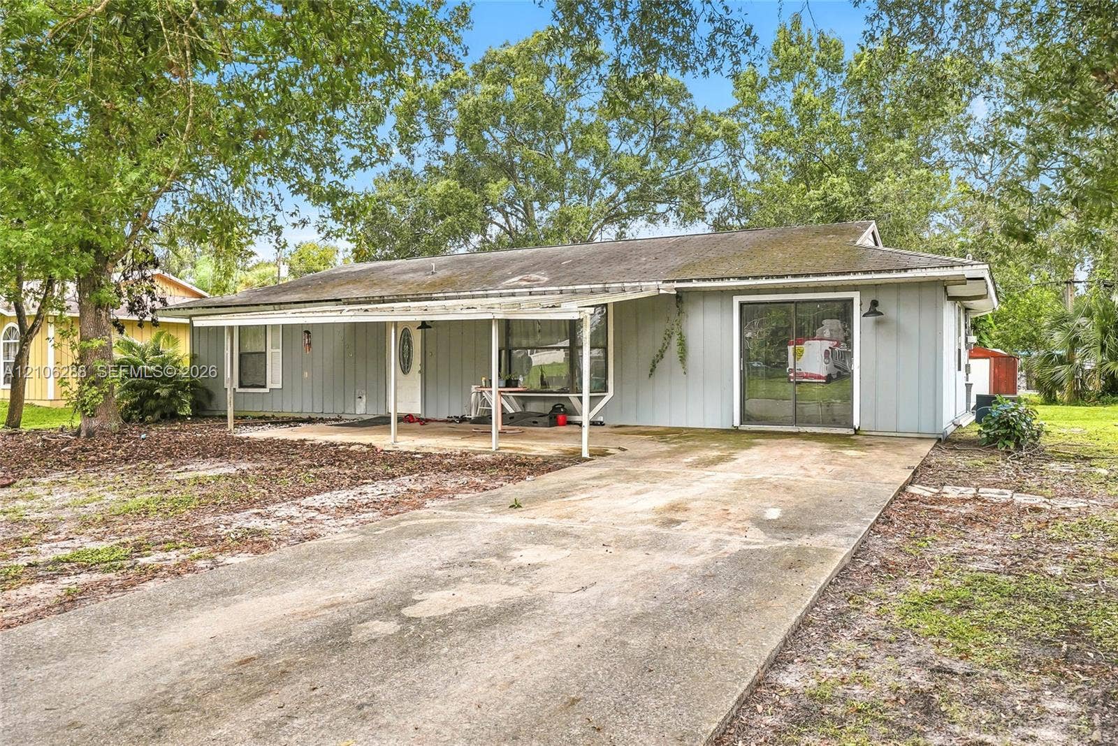 Single-story residence featuring vertical siding, a covered front porch, concrete driveway, and sliding glass door entrance