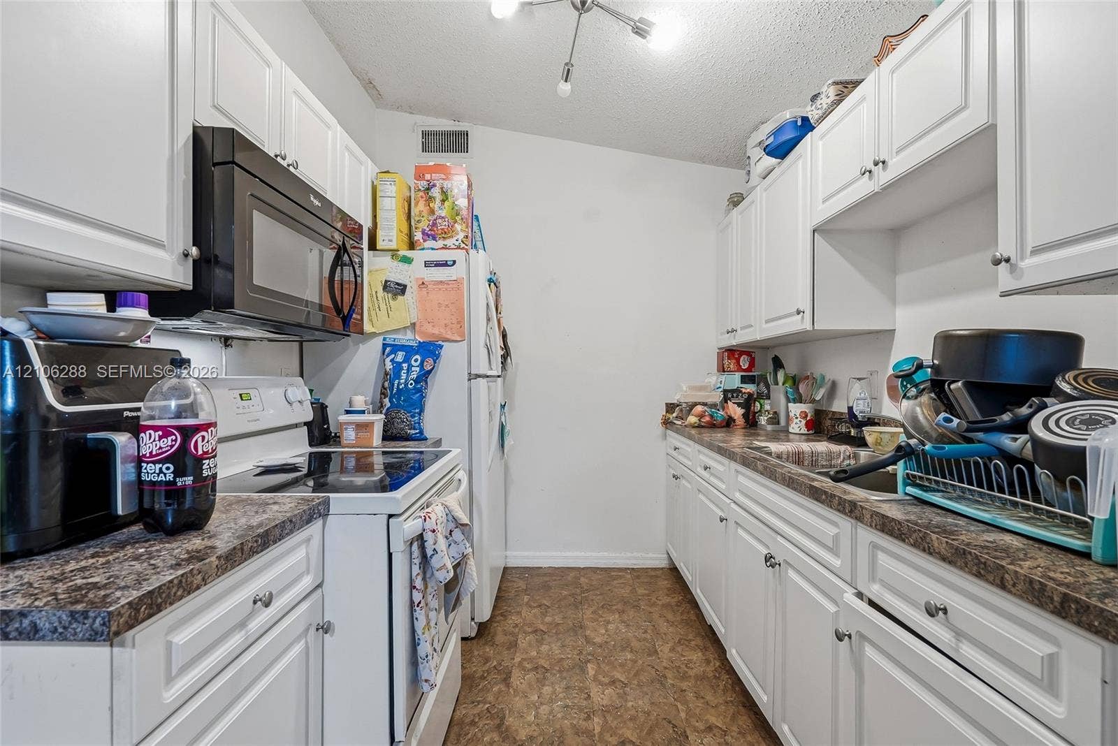 Kitchen featuring white raised-panel cabinetry, stone-finish countertops, black microwave, and multi-arm ceiling lighting