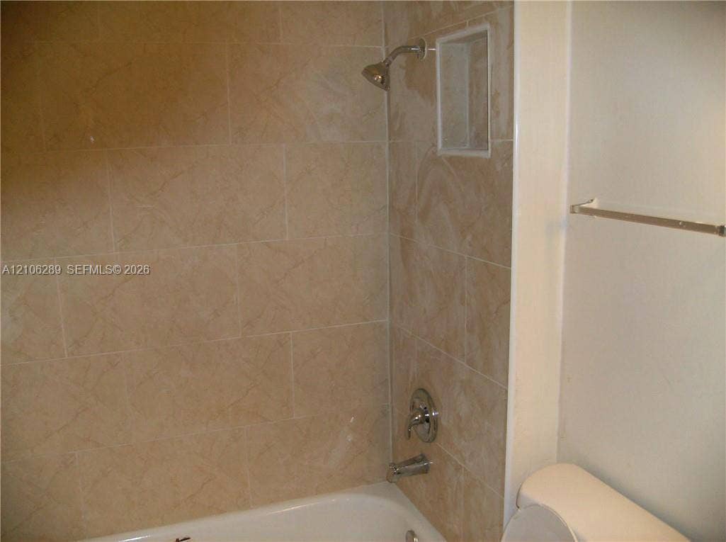 Bathtub enclosure featuring large-format ceramic tile surround, integrated shower niche, chrome plumbing fixtures, and wall-mounted metal towel bar