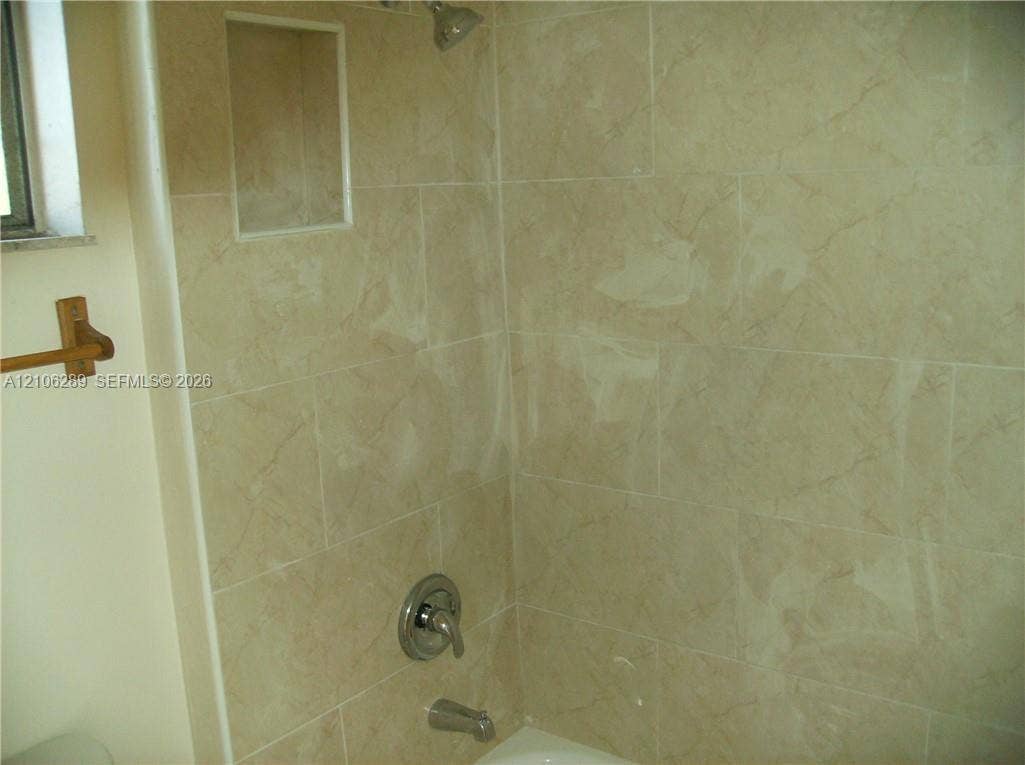 Full-height ceramic wall tiling featuring a neutral veined pattern, integrated recessed shelving, and a brushed metallic shower and tub faucet set