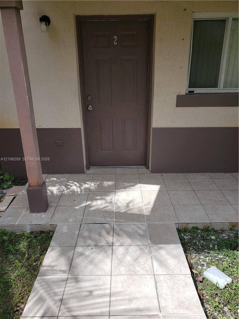 Entrance featuring a four-panel door, tiled patio, and exterior wall-mounted lighting fixture