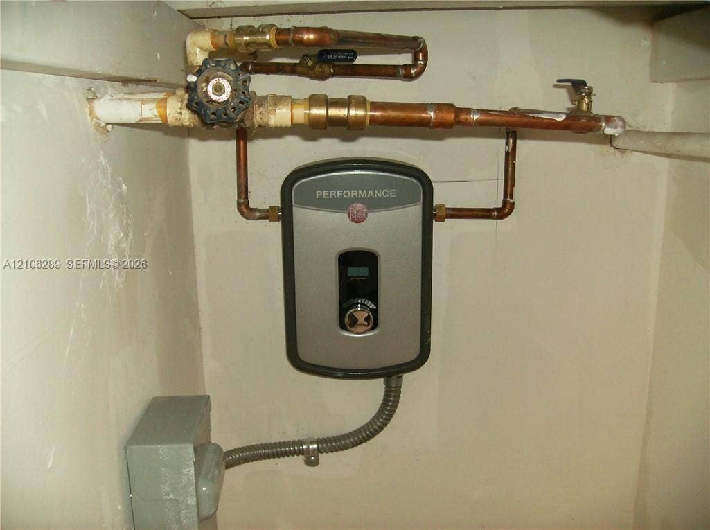 Tankless electric water heater featuring digital temperature controls, copper plumbing lines, and a shut-off valve