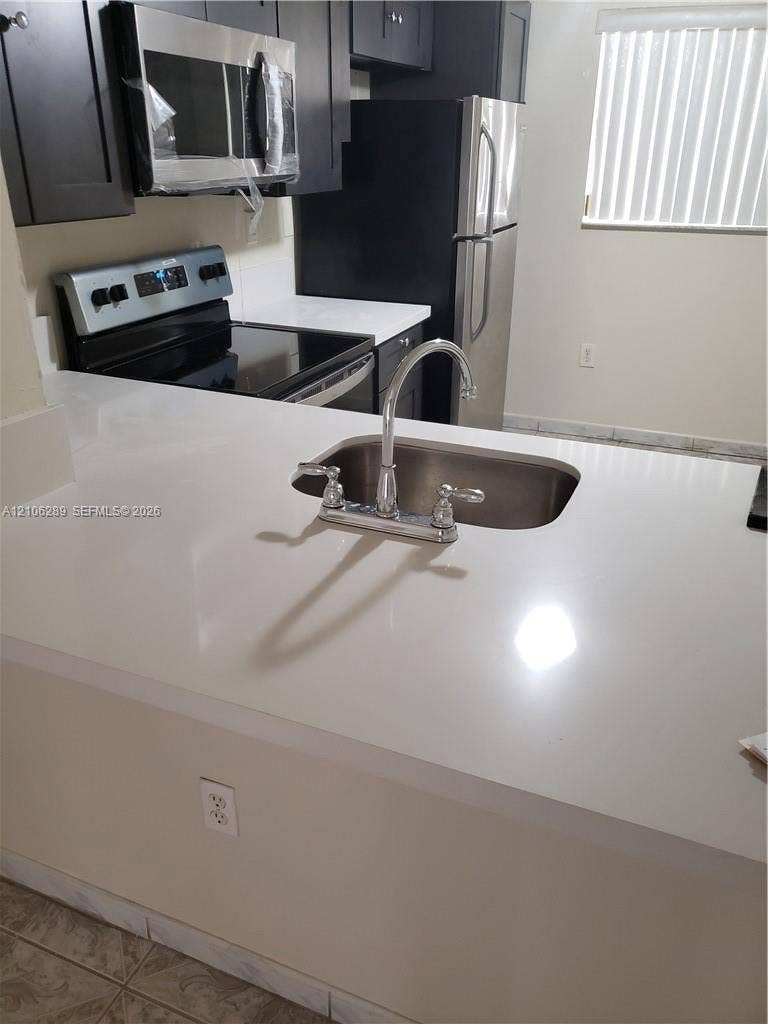 Kitchen featuring an expansive countertop, stainless steel sink with high-arch faucet, dark cabinetry, and stainless steel appliances