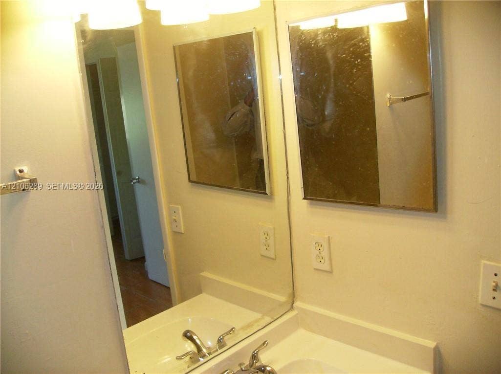 Integrated vanity with a white countertop and recessed basin, wall-mounted mirror, metal faucet hardware, and multi-bulb overhead light fixture