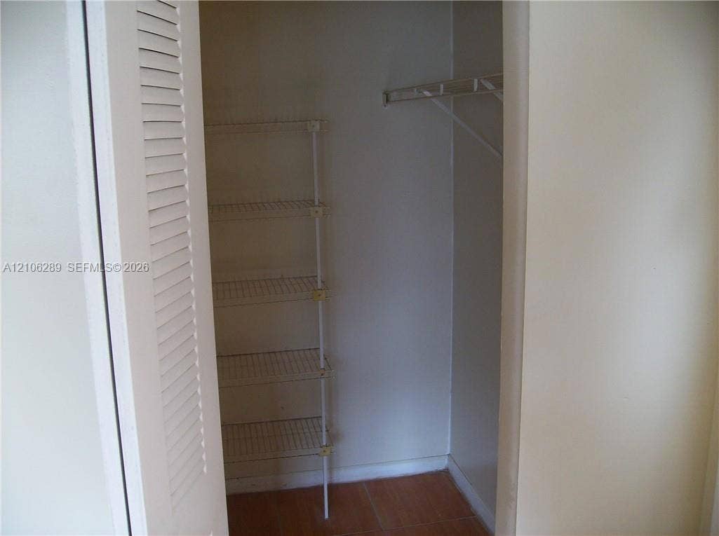 Reach-in closet featuring louvered bi-fold doors, white wire shelving, and tile flooring