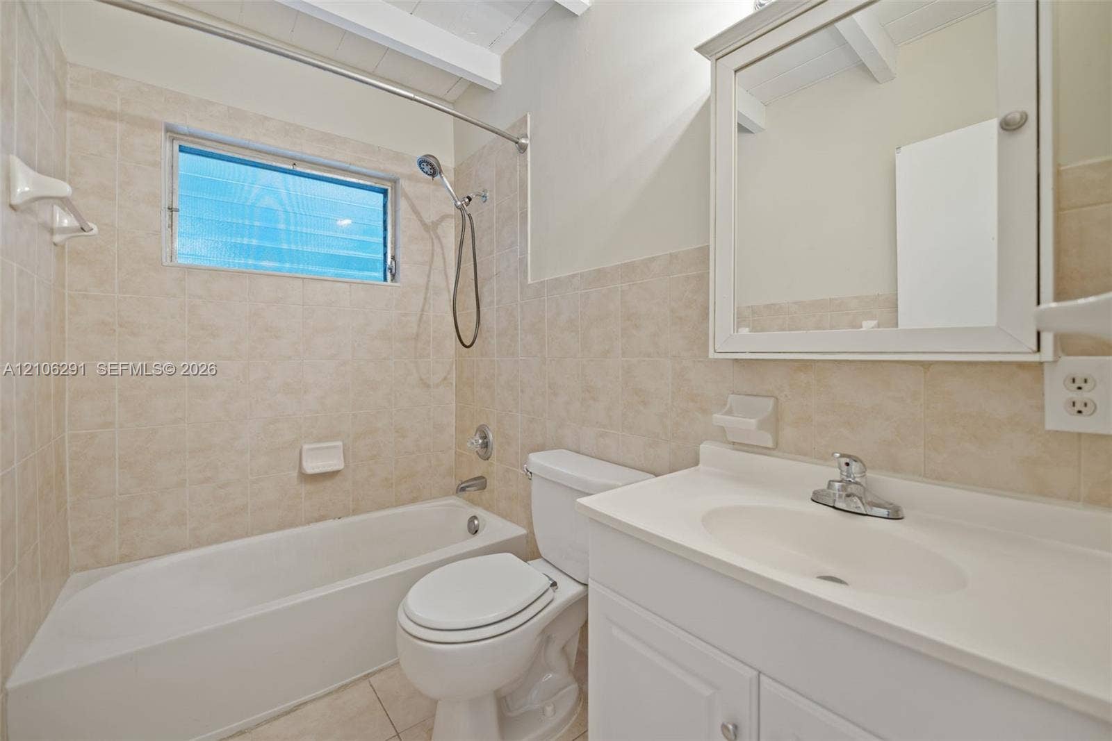 Bathroom featuring tile tub surround, integrated vanity sink, mirrored medicine cabinet, exposed wood-beam ceiling, and porcelain tile flooring