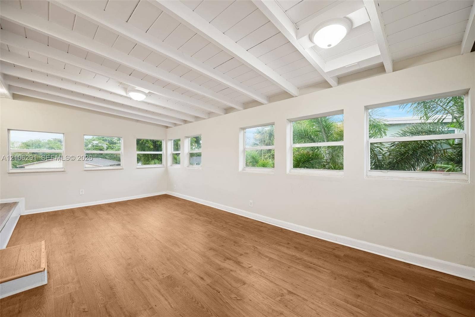 Exposed white-painted ceiling beams, wood-finish flooring, and multiple windows providing natural light