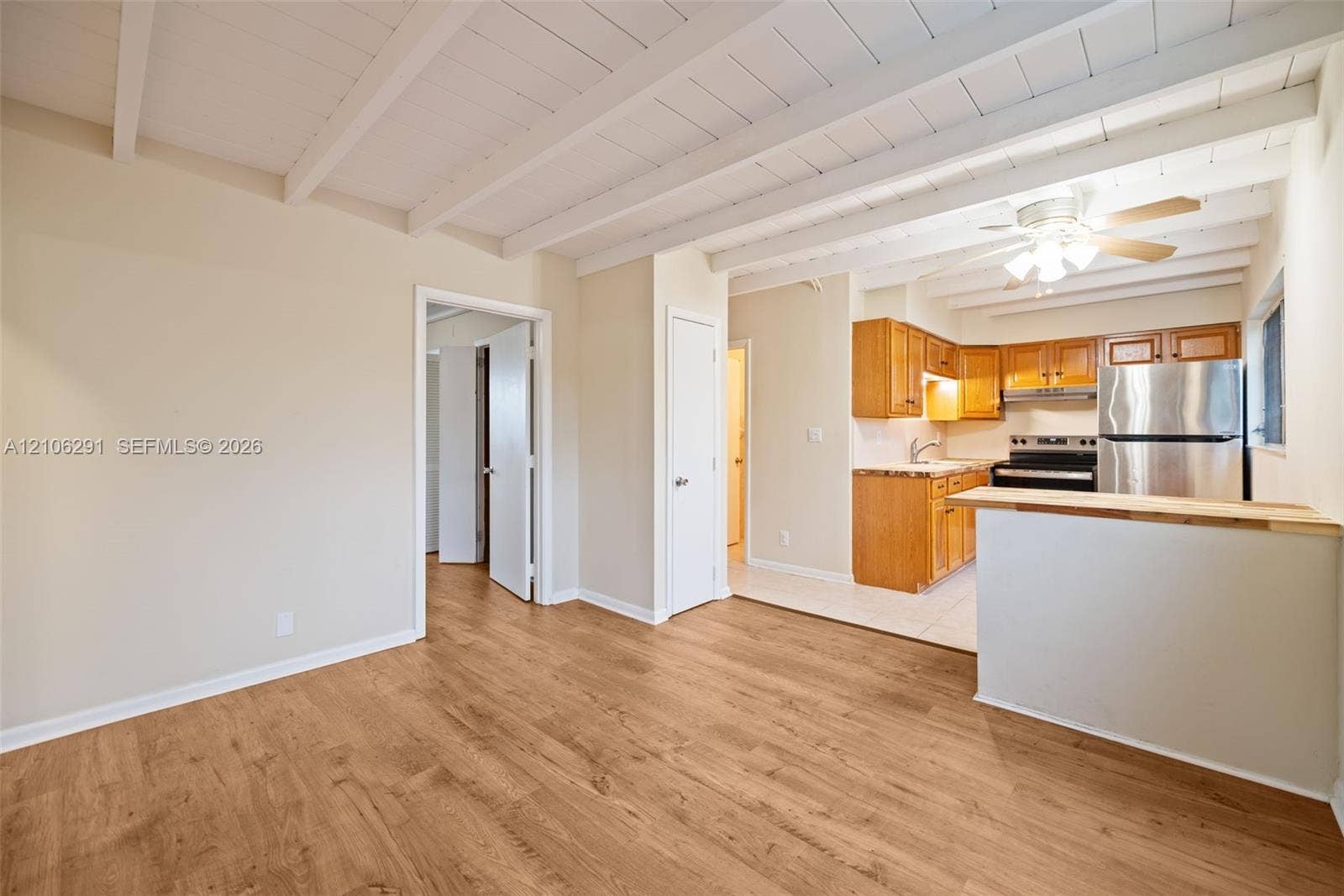 Exposed beam ceiling featuring white-painted finish, wood-finish flooring, and kitchen area with natural wood cabinetry, stainless steel refrigerator, and peninsula