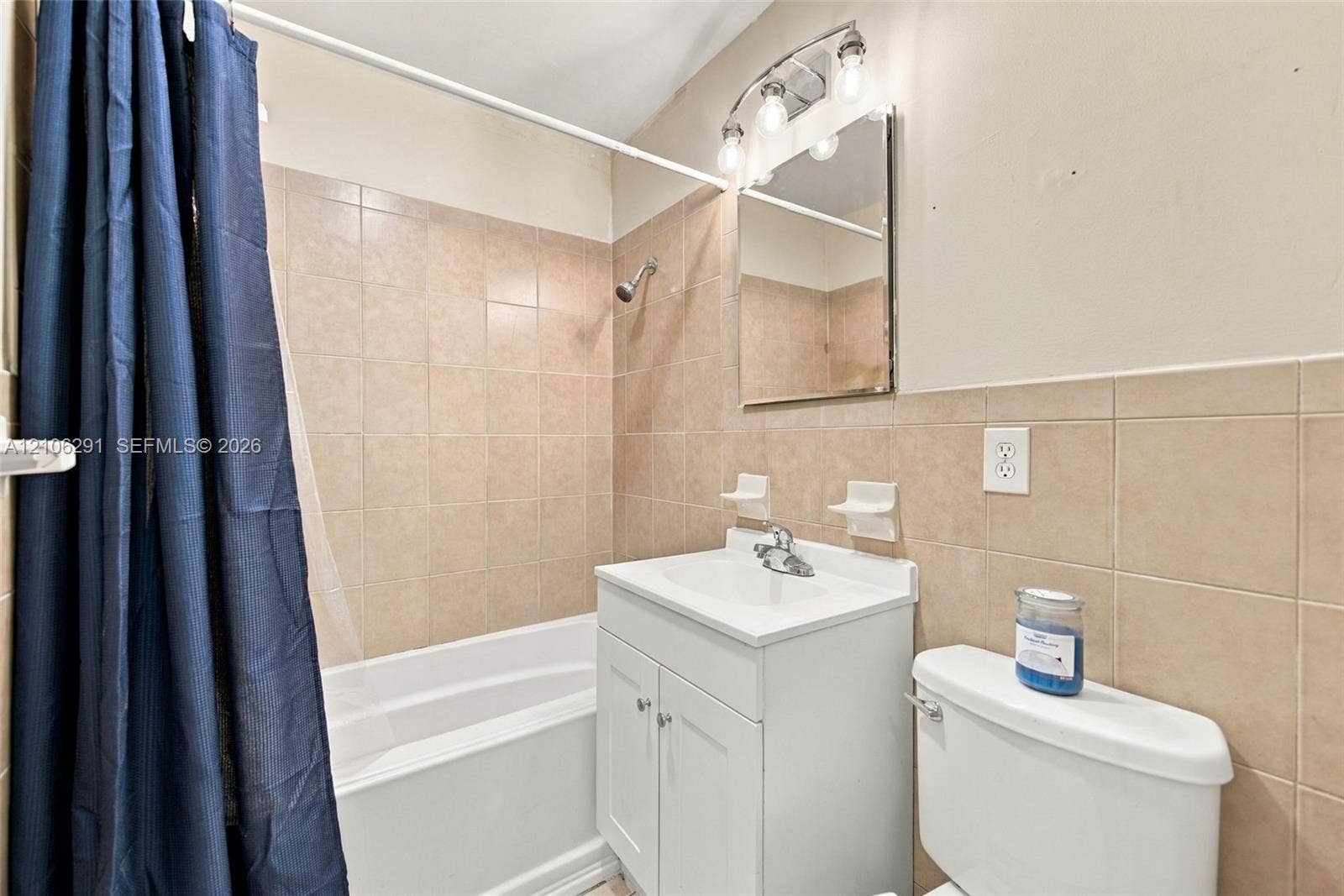 Bathroom featuring square wall tiling, a white vanity with an integrated sink, a frameless medicine cabinet, and a multi-bulb light fixture