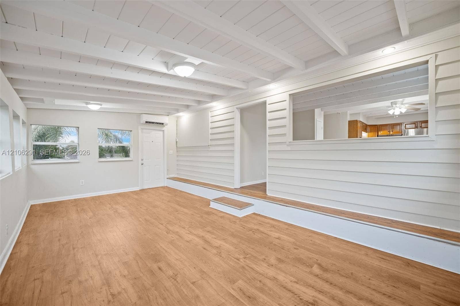 Interior featuring exposed beam ceilings, wood-finish flooring, horizontal shiplap wall paneling, a tiered floor elevation, and a rectangular pass-through opening