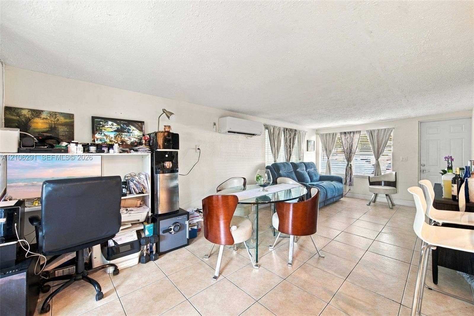 Open-concept interior featuring neutral tile flooring, wall-mounted ductless climate control system, and large windows with horizontal blinds
