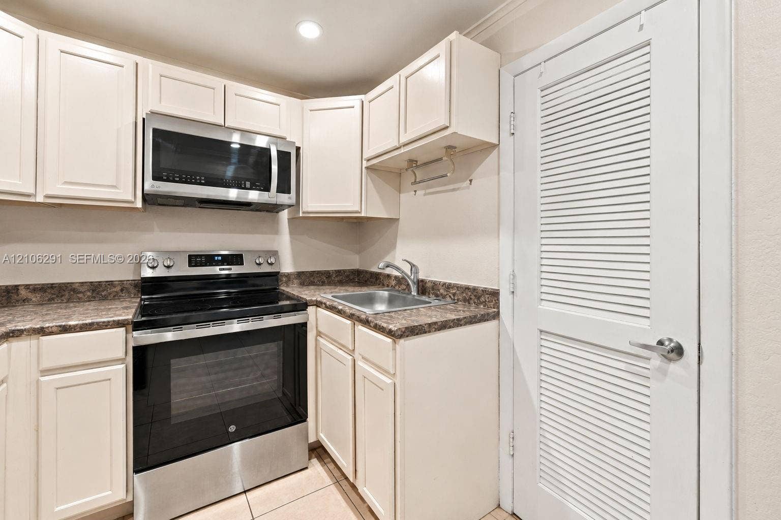 Kitchen featuring white cabinetry, stainless steel appliances, speckled laminate countertops, a single-basin sink, and tile flooring