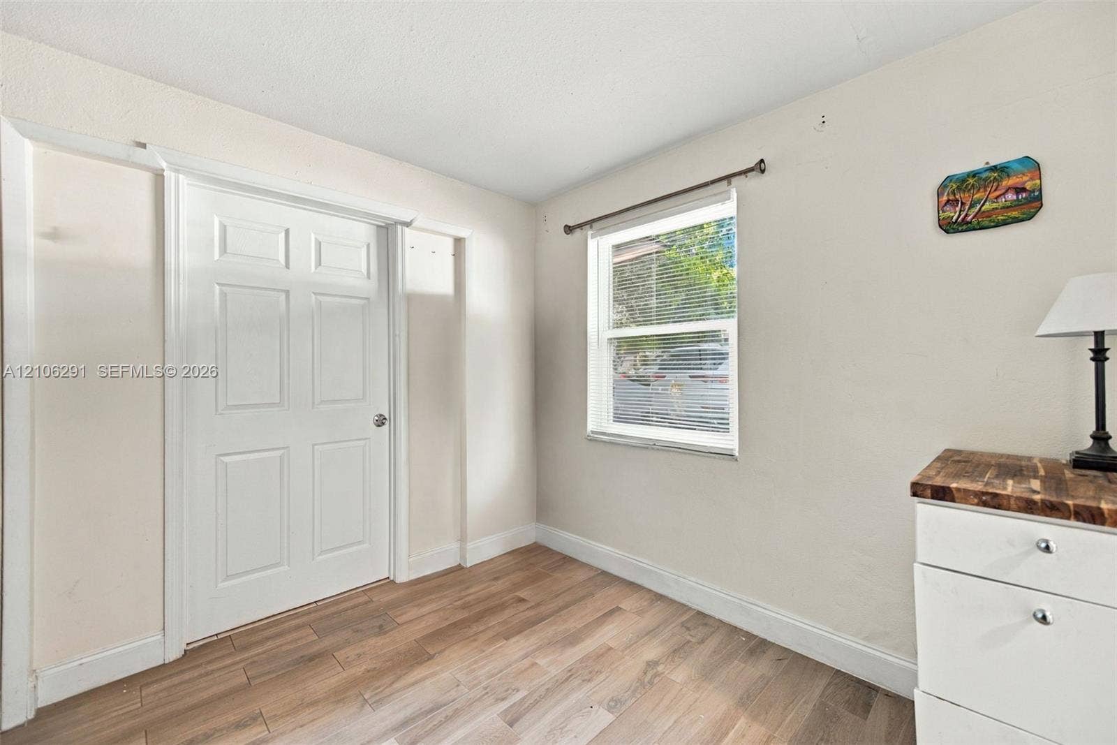 Room featuring wood-finish flooring, a single-panel interior door with casing, and a window with a metal curtain rod