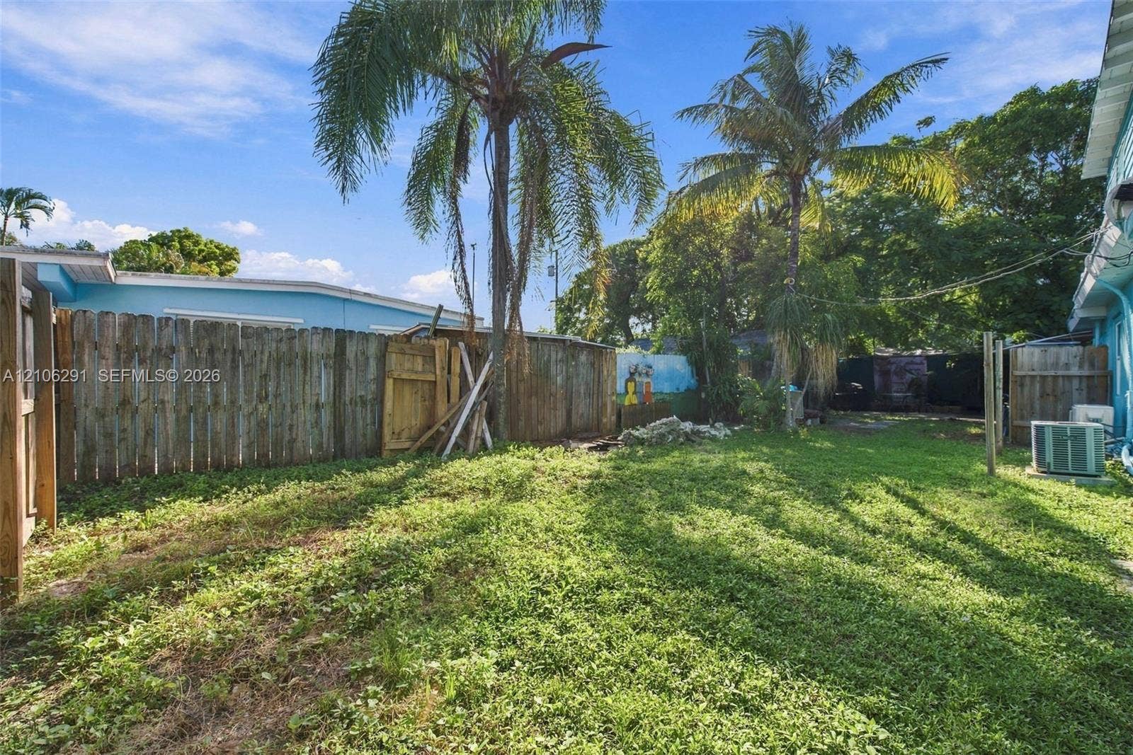 Backyard featuring a wood-panel perimeter fence, mature palm trees, and an exterior HVAC unit