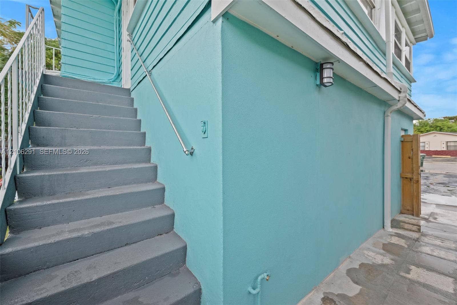 Exterior featuring painted lap siding, concrete staircase with metal handrails, wall-mounted outdoor lighting, and paved ground surface