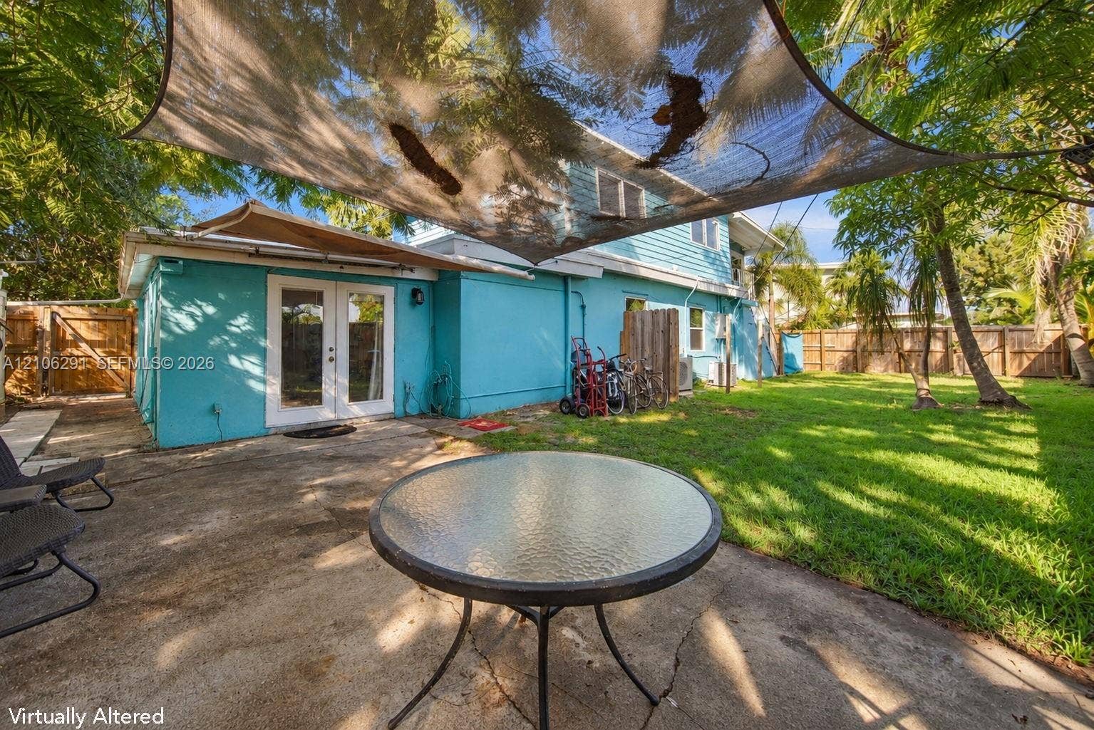 Backyard featuring a concrete patio, shaded seating area with a tensile canopy, mature trees, and perimeter wood fencing