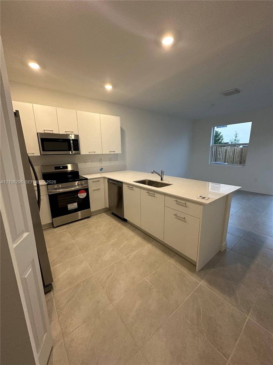 12103 NW 24th Place, #12103, Miami, Miami, FL 33167 Kitchen featuring white flat-panel cabinetry, light-toned stone-finish countertops, stainless steel appliances, and large-format tile flooring