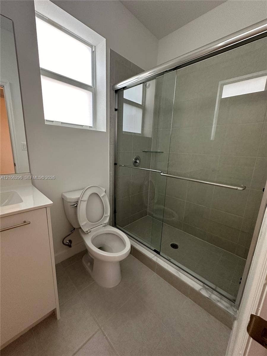 12103 NW 24th Place, #12103, Miami, Miami, FL 33167 Bathroom featuring a white vanity with a rectangular sink, walk-in shower with a glass sliding enclosure and tiled surround, and large-format neutral floor tile