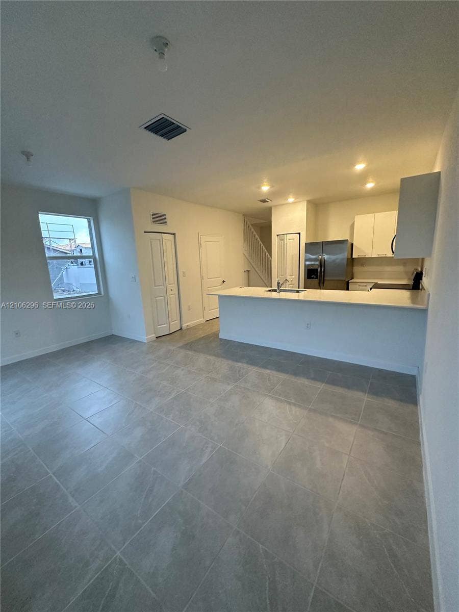12103 NW 24th Place, #12103, Miami, Miami, FL 33167 Open-concept kitchen featuring a breakfast bar with solid-surface countertops, stainless steel refrigerator, white cabinetry, and large-format tile flooring