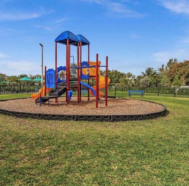 12103 NW 24th Place, #12103, Miami, Miami, FL 33167 Outdoor recreational area featuring a multi-level playground structure, wood chip surface, metal perimeter fencing, and open green space