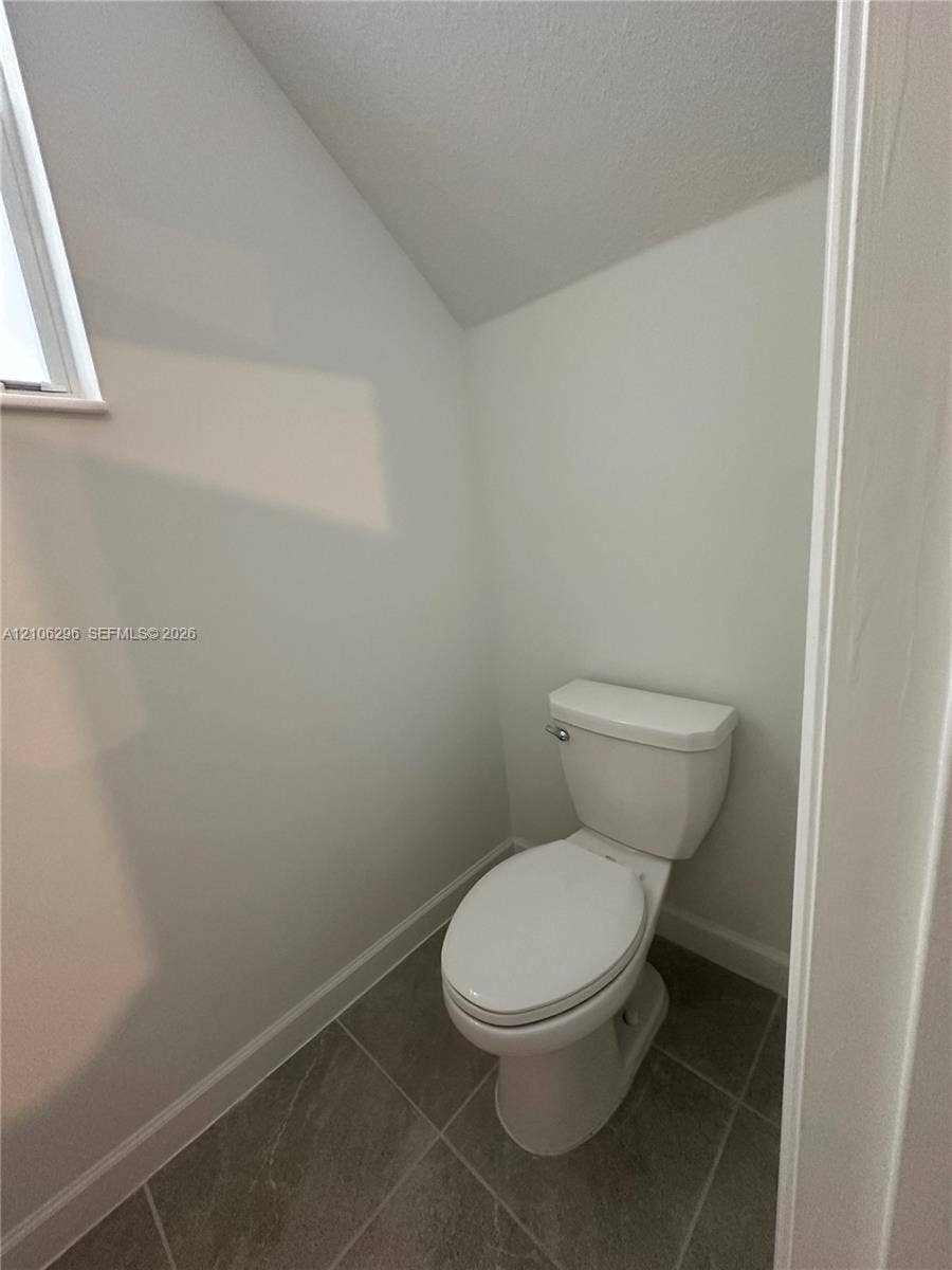 12103 NW 24th Place, #12103, Miami, Miami, FL 33167 Enclosed space featuring porcelain toilet, tile flooring, and angled ceiling