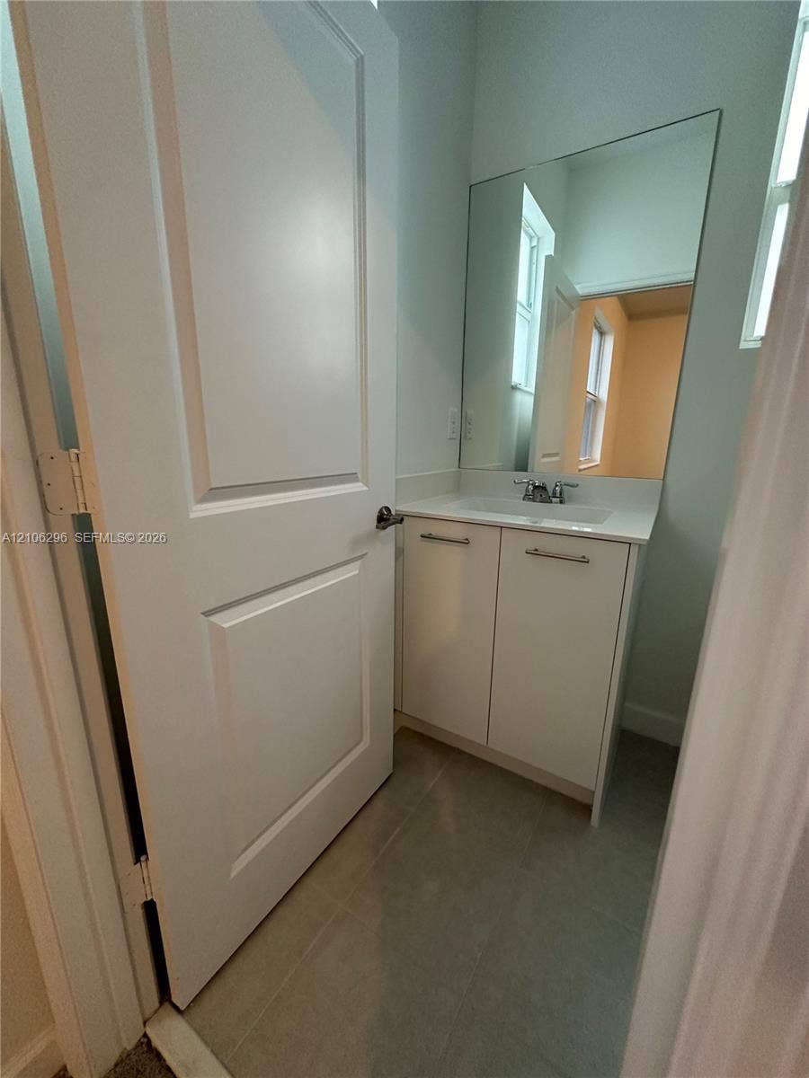 12103 NW 24th Place, #12103, Miami, Miami, FL 33167 White shaker-style vanity with a solid surface countertop, rectangular integrated sink, chrome hardware, and large wall-mounted mirror