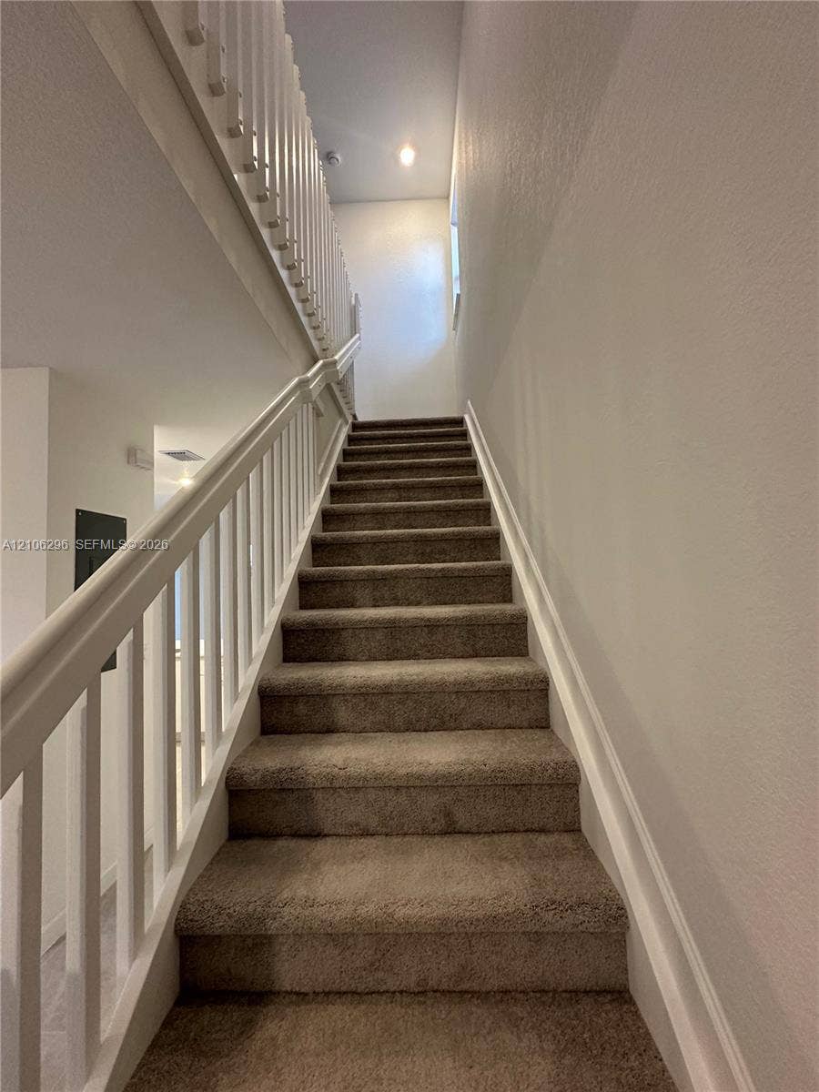 12103 NW 24th Place, #12103, Miami, Miami, FL 33167 Staircase featuring neutral carpeting, a white wooden handrail, and a white balustrade