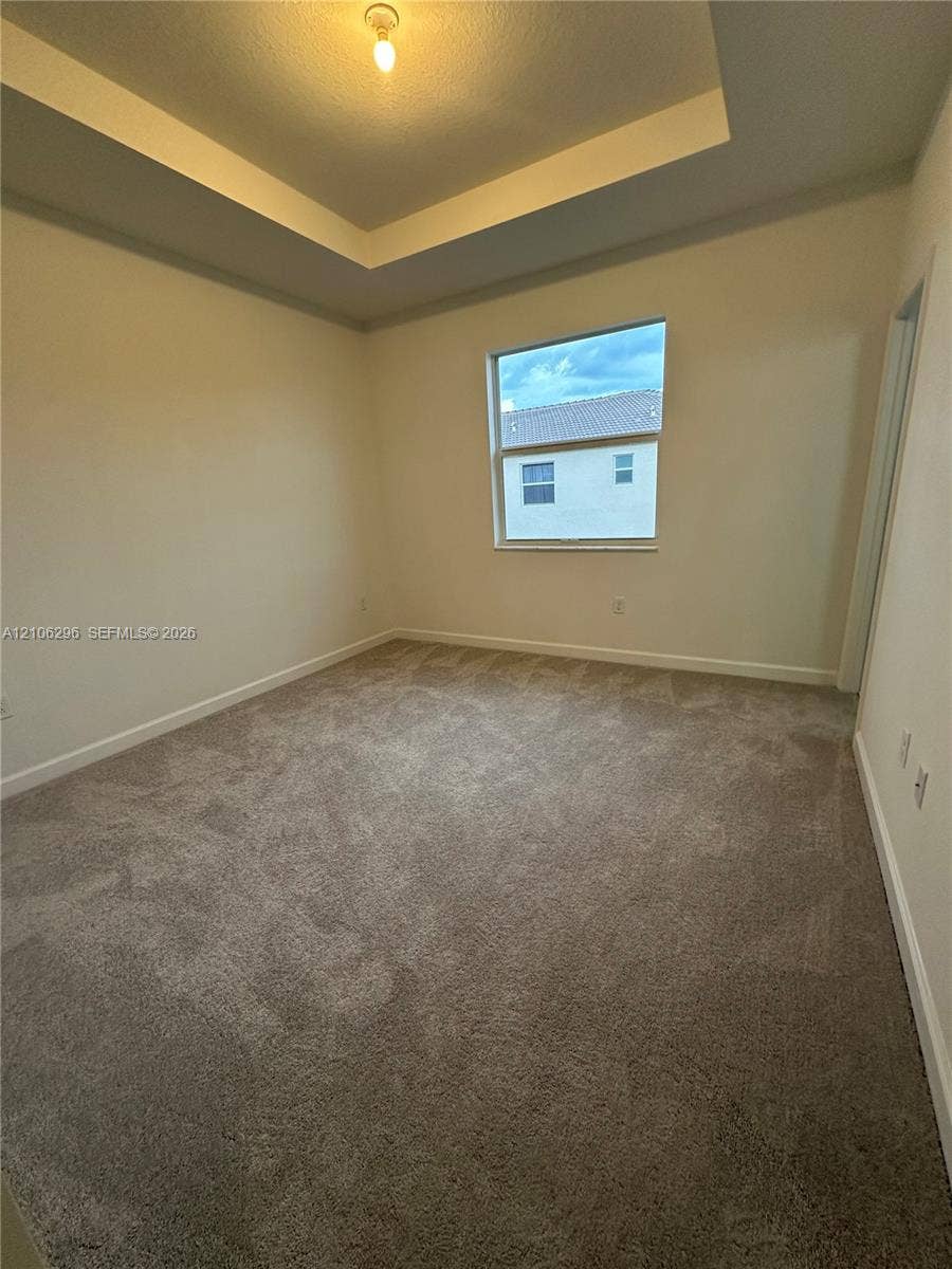 12103 NW 24th Place, #12103, Miami, Miami, FL 33167 Room featuring a tray ceiling, neutral-toned wall-to-wall carpeting, and a single-pane window